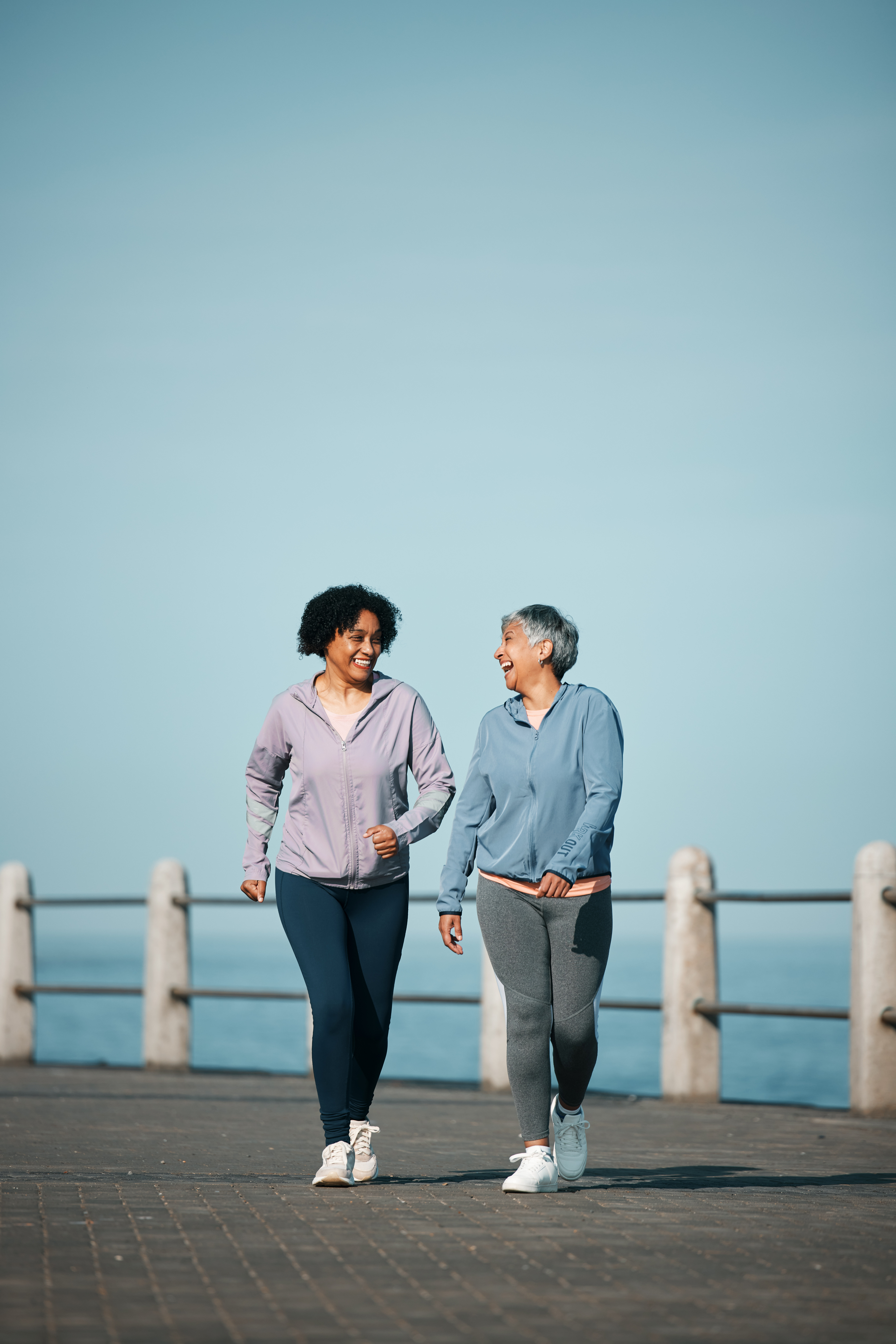 exercise, walking and senior women by ocean for healthy body, wellness and cardio on promenade. sports, friends and happy female people in conversation on boardwalk for fitness, training and workout