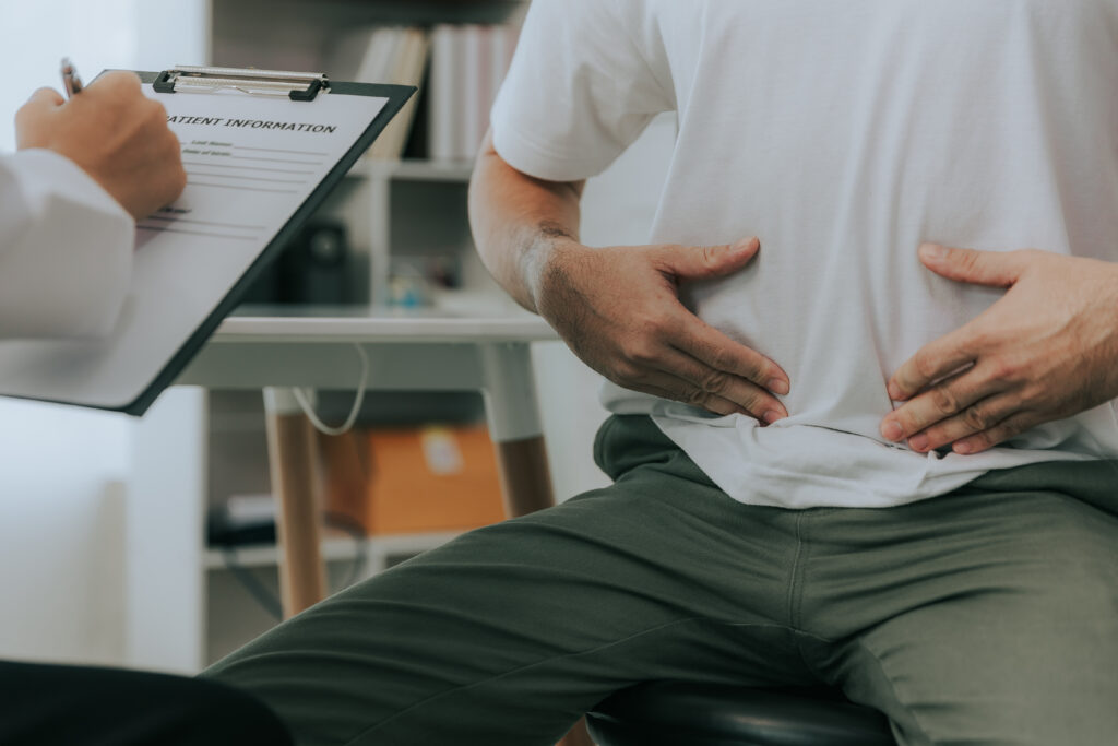 crohn's disease or ulcerative colitis concept. doctor counseling male patient with abdominal pain in hospital examination room