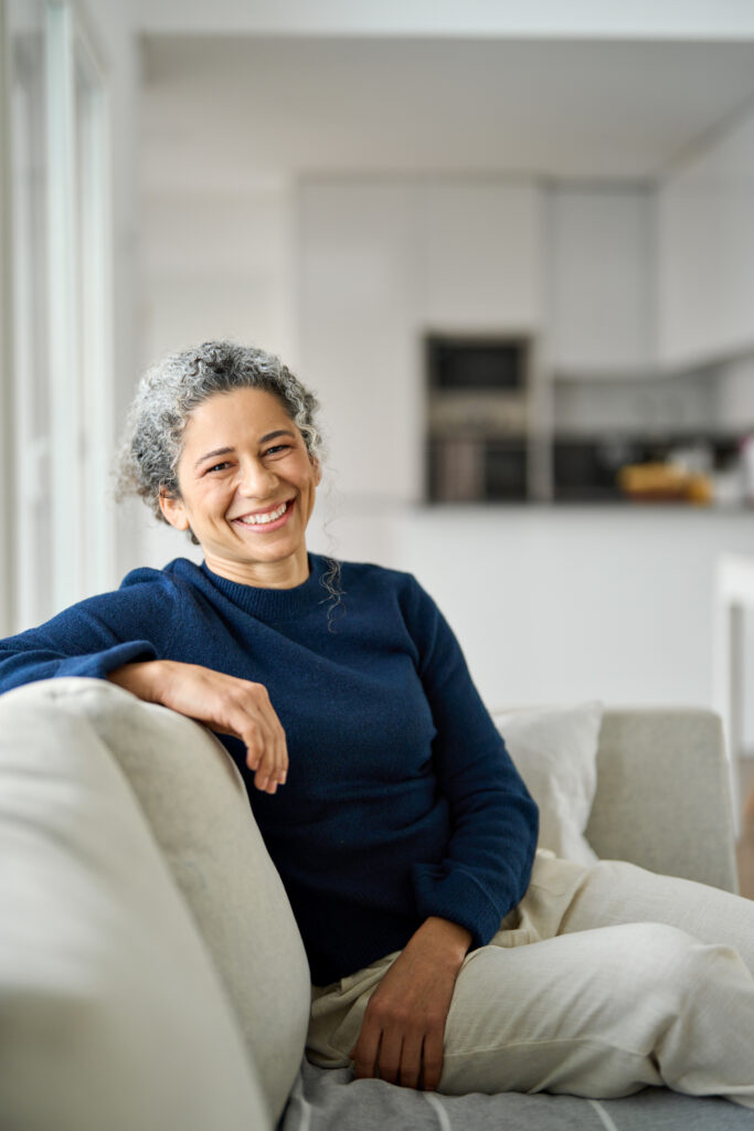 happy mature woman sitting on sofa in living room at home. vertical portrait.
